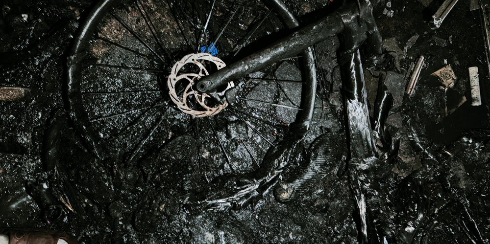 Charred bicycle wheel with white disc brake rotor and burnt black frame remnants symbolizing xie cuifeng cycling family spirit