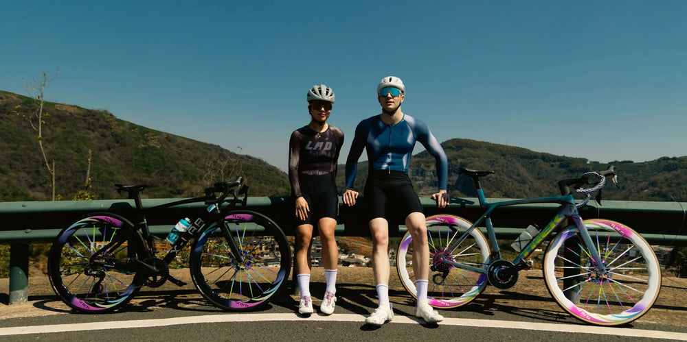 Two cyclists in matching blue and black cycling jerseys with rainbow wheels illustrate cycling apparel differences.