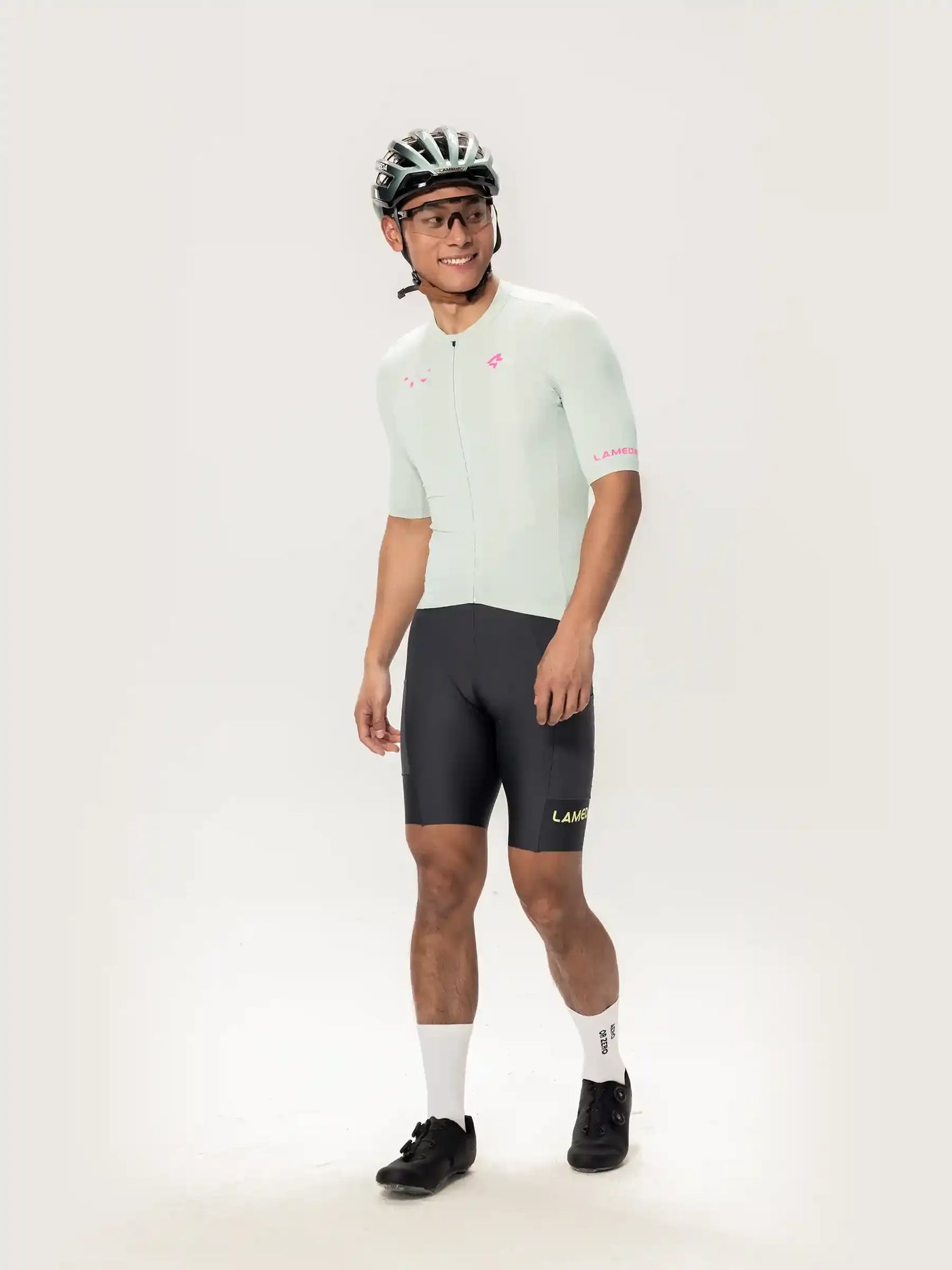 Modellen bär en ljus myntgrön kortärmad Roam Men cykeltröja med rosa märkning och svarta shorts med lamer-logotyp