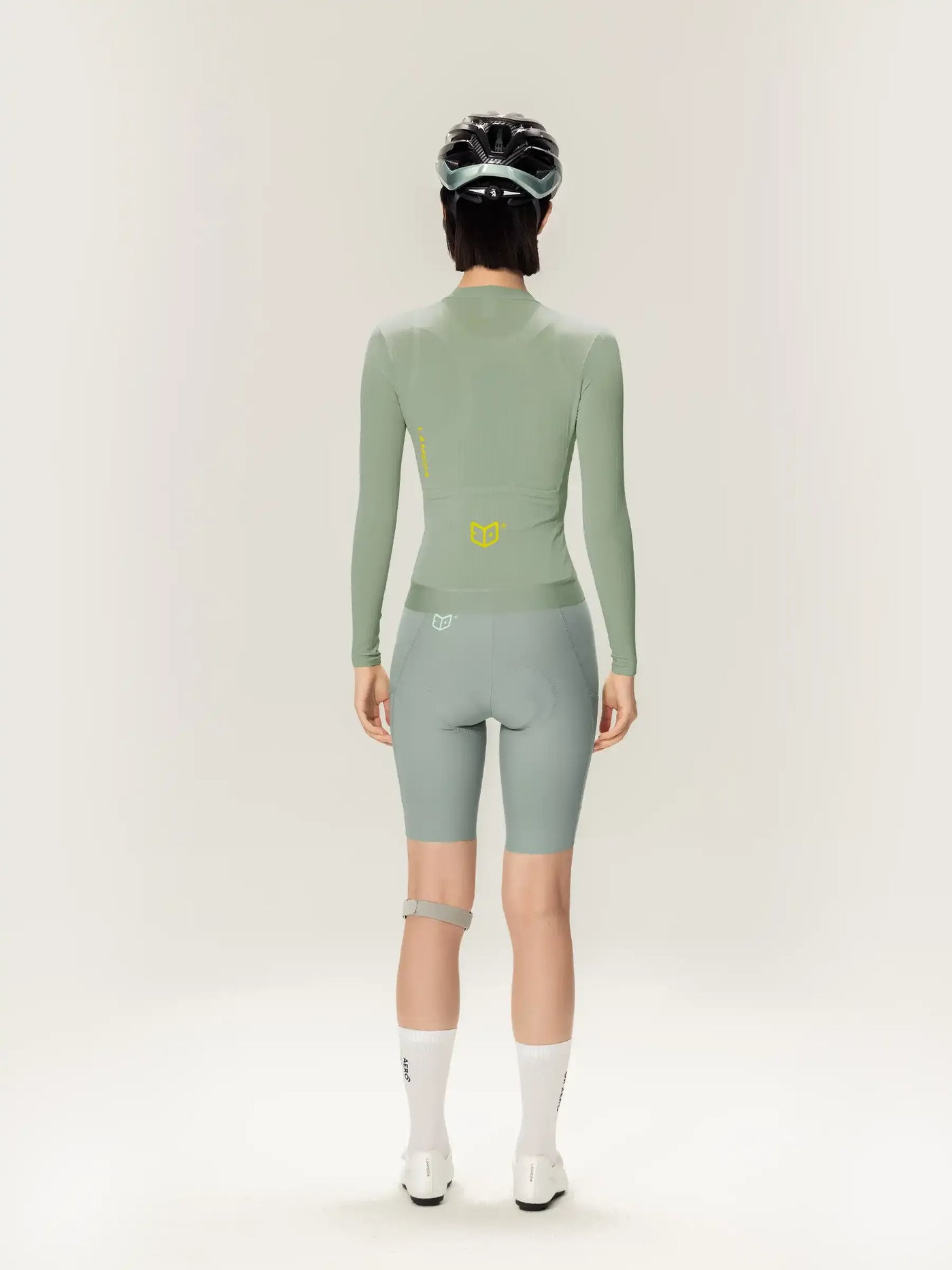 Baksida av en slank salviagrön roam långärmad damcykeltröja med diskret gul logotyp och matchande shorts
