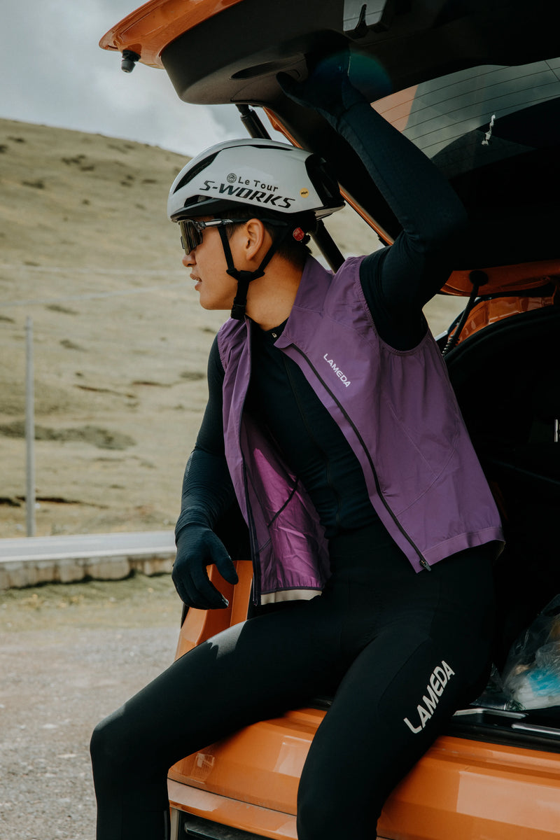 Person wearing a helmet and purple vest sitting on an orange vehicle with a mountainous background.