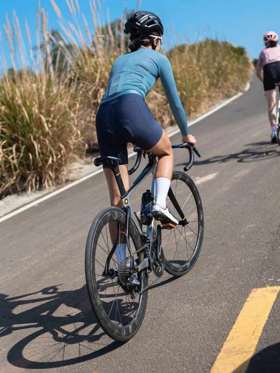 Svart vägcykel med strömlinjeformad aerodynamisk ram och fallhandtag visas bredvid navy jade damcykelbibshorts