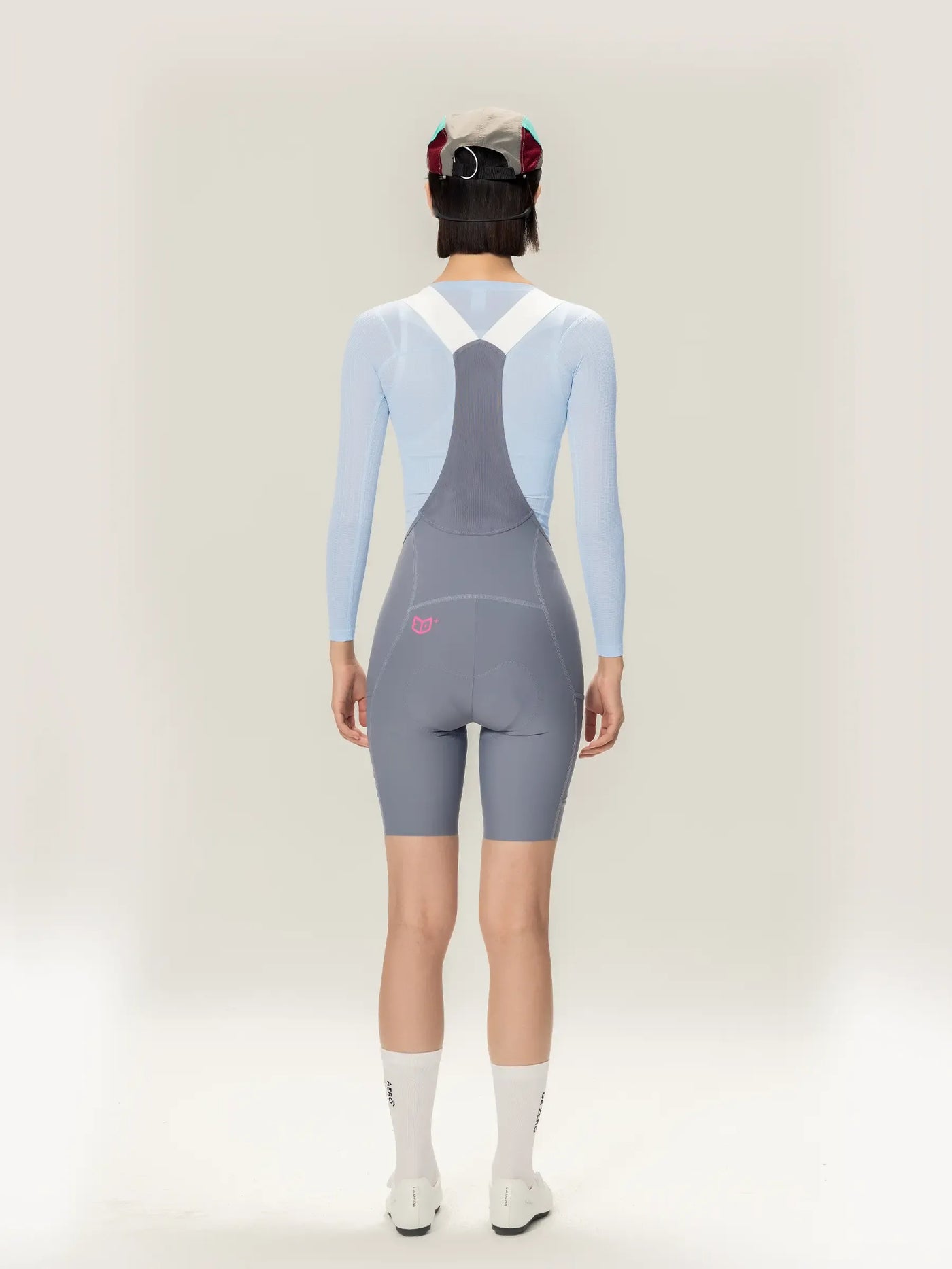 Bakvy av grå cykelhängbyxor med vita remmar och rosa logotyp kombinerat med lightweave blå långärmad dambaslager med airflow mesh för LAMEDA clouds damcykeltanktopp