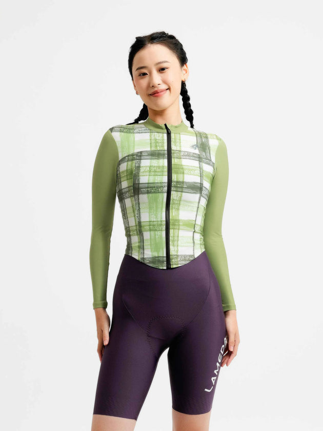 En kvinna som bär en grön LAMEDA prismatic damcykeltröja med svart dragkedja och lila cykelshorts