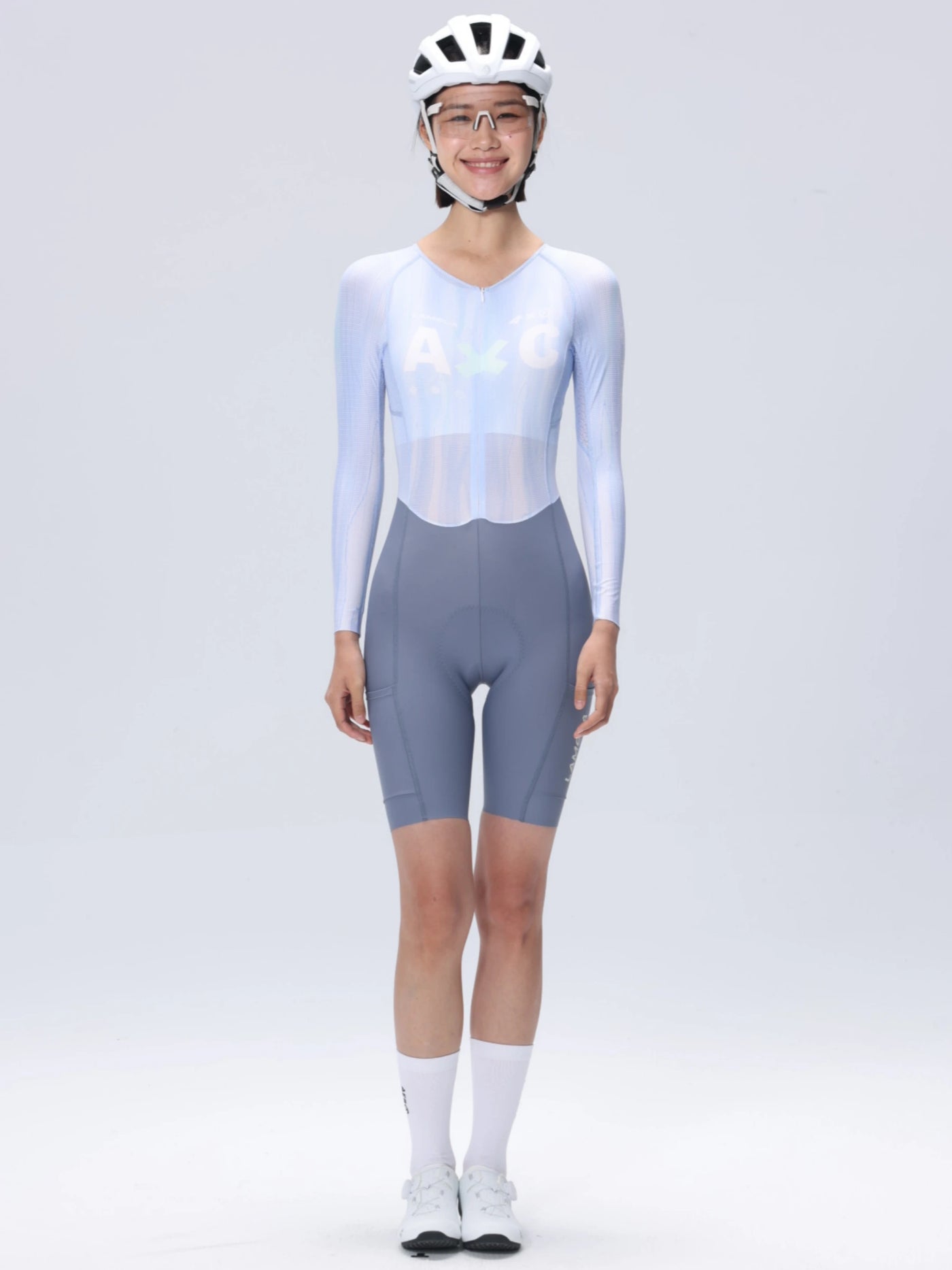 En kvinna som bär vit cykelhjälm och ljusblå långärmad LAMEDA A*C dam skinsuit för cykling