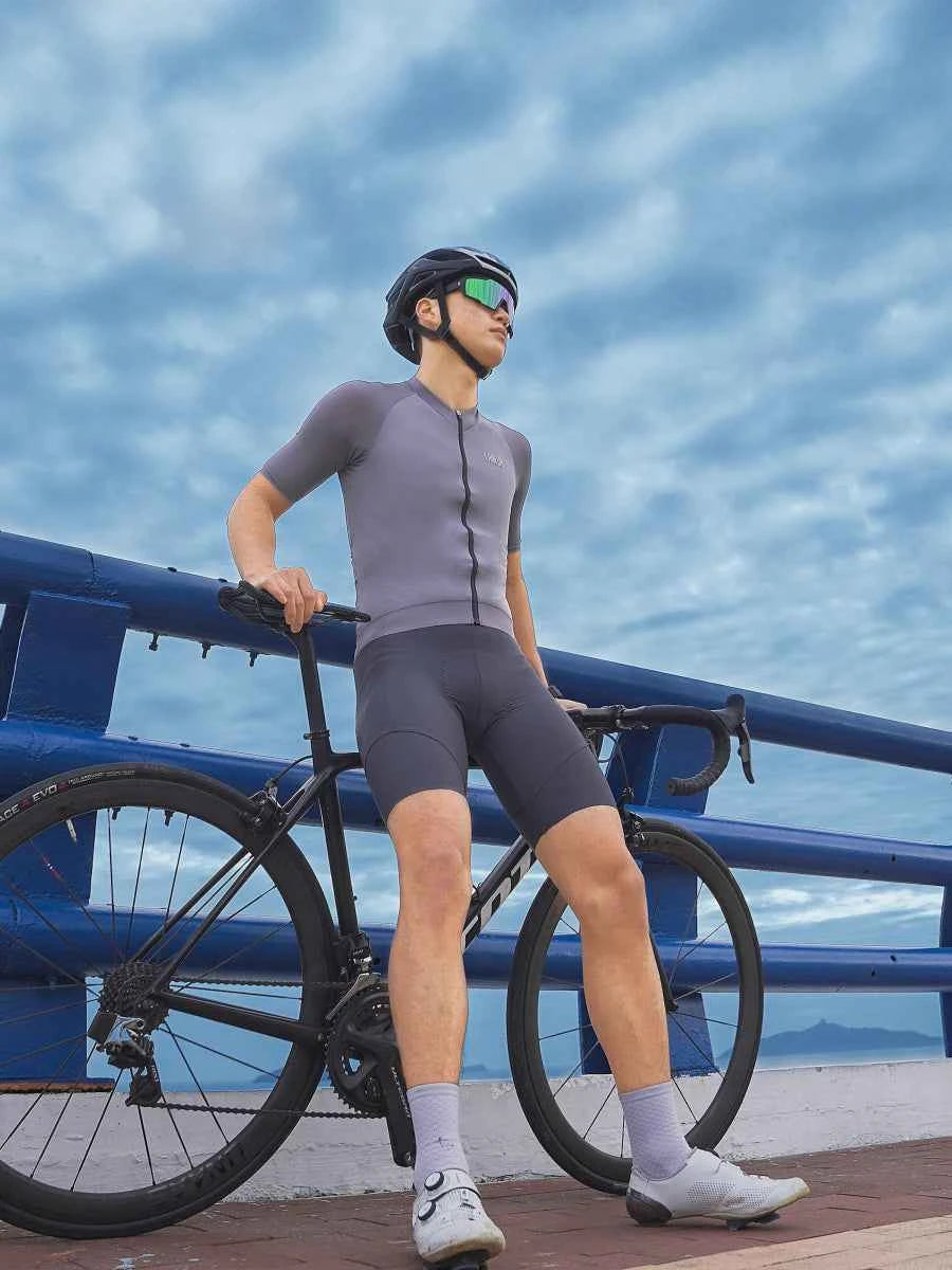 Grå LAMEDA mody kortärmad cykeltröja med svart blixtlås bärs av cyklist bredvid cykel i mody lila linje