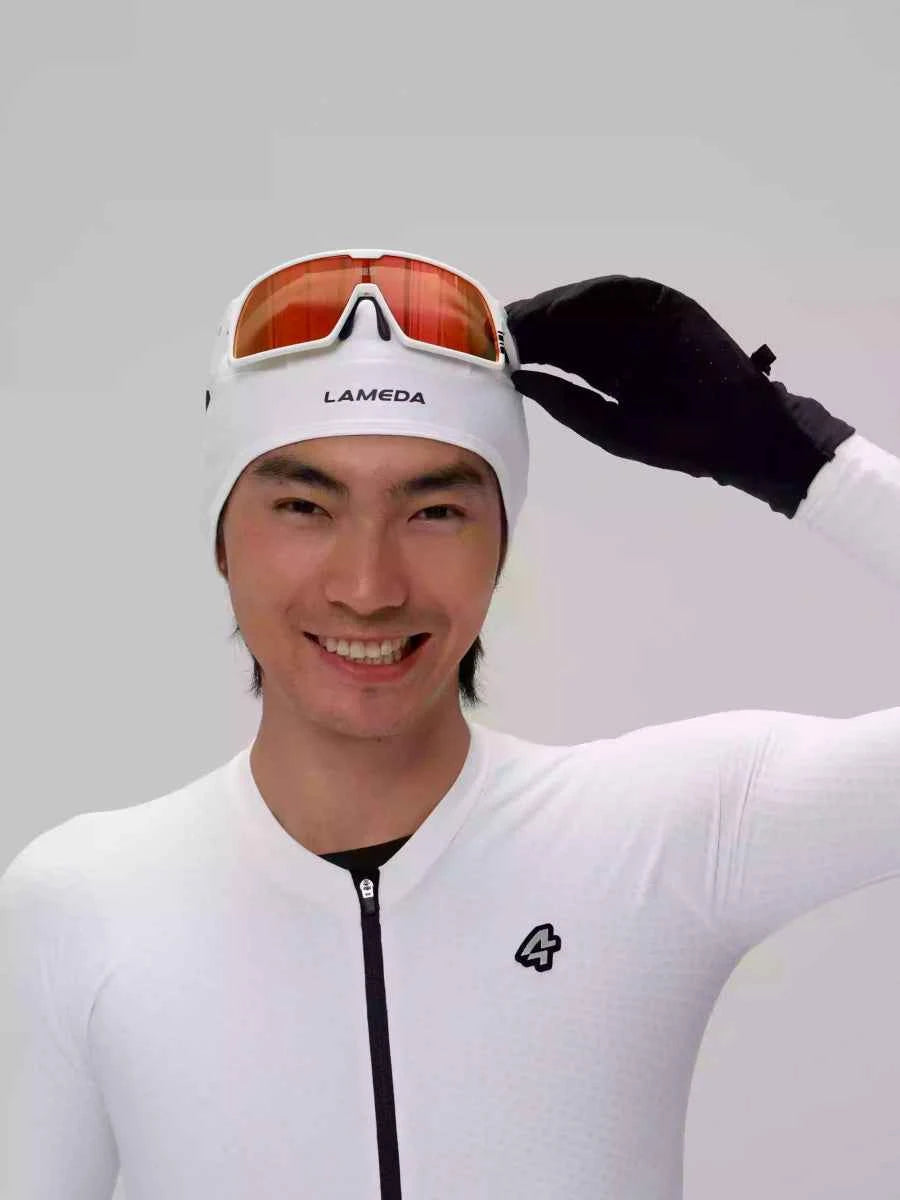 Weiße Lameda Thermofleece-Helmunterziehmütze für unter den Fahrradhelm, mit orange-getönten Gläsern und schwarzen Handschuhen für warme Radtouren