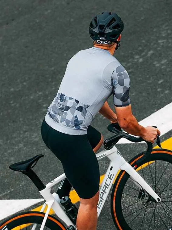 En strömlinjeformad vit cykel med orange fälgar och svart sadel bredvid en blå cykeltröja i relaxed fit av ispace