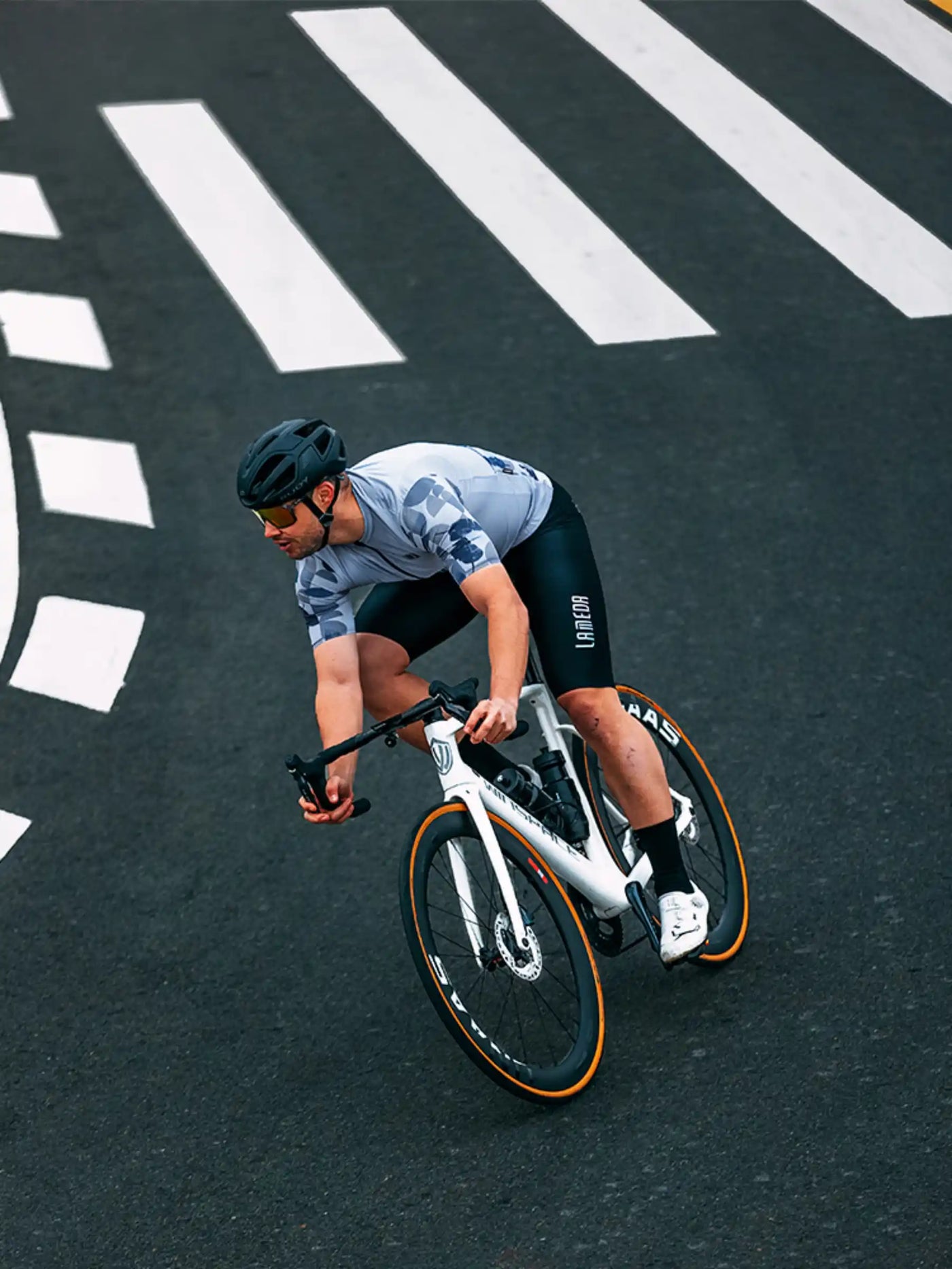 Vit landsvägscykel med hjul med orange fälgar och svarta styren bredvid blå cykeltröja i avslappnad passform för män