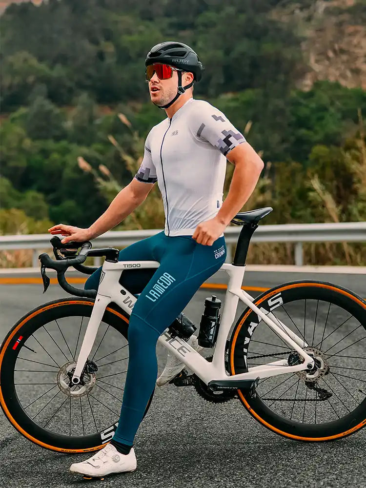 Vit och orange vägcykel med svarta cykelstyre bredvid vit herr cykeltröja med avslappnad passform och blågröna cykelshorts