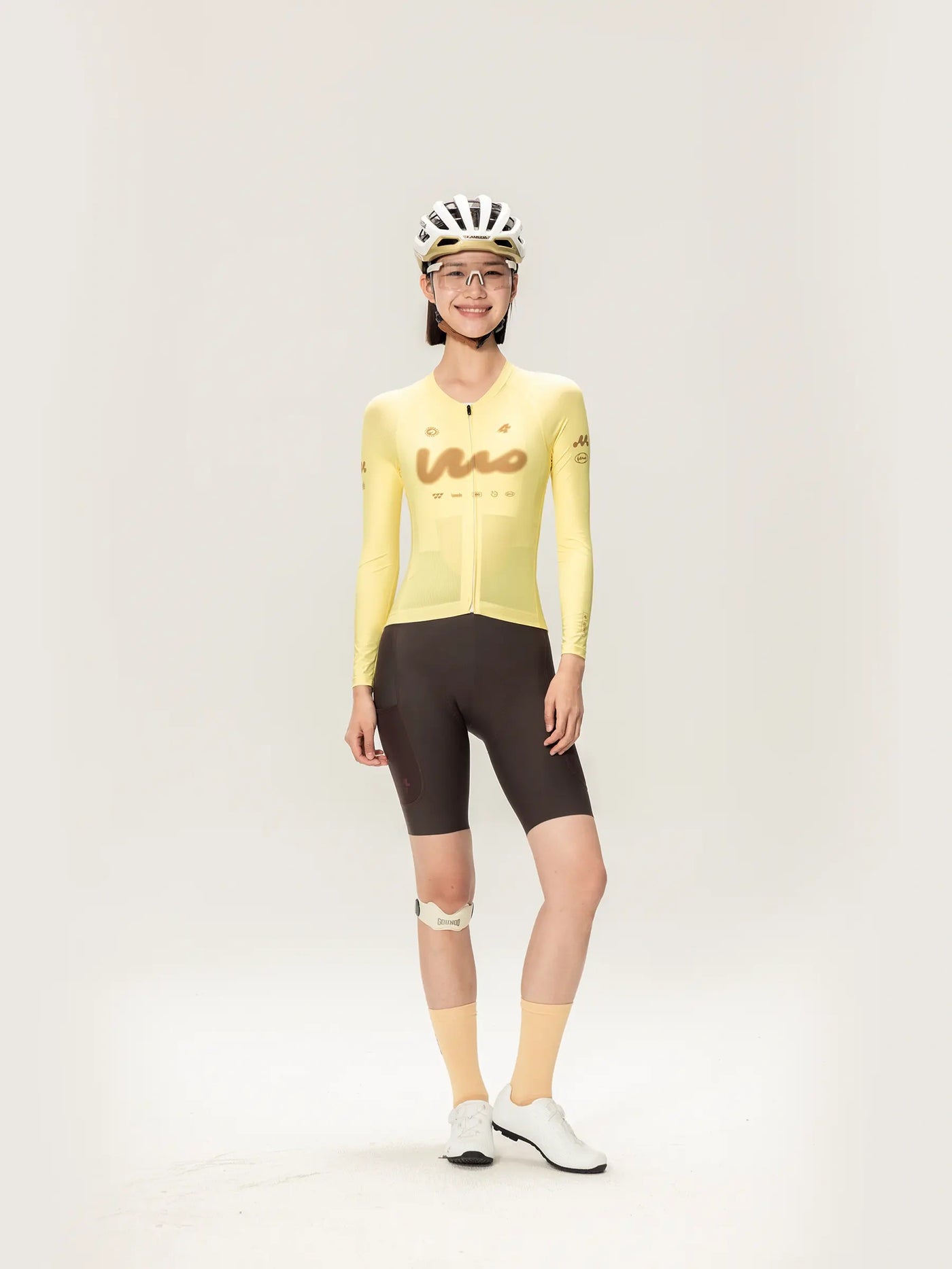 En kvinna bär en gul LAMEDA damcykeltröja med långa ärmar ihop med svarta shorts och matchande tillbehör